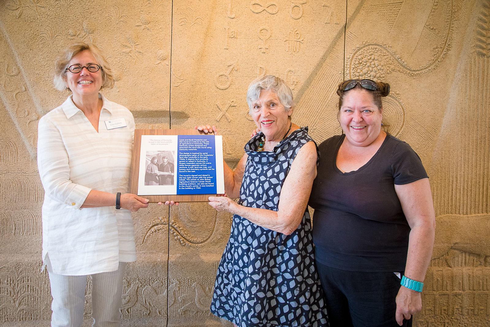 women with certificate in front of sandstone mural